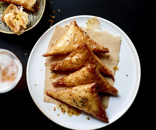 Four folded pastry triangles on a piece of brown paper, laid on a white round plate, on a black background.