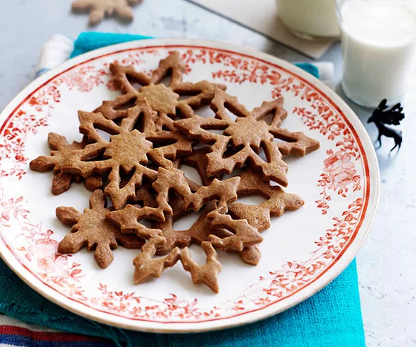 A round white plate, with an ornamental red floral border, holding star-shaped baked cookies.