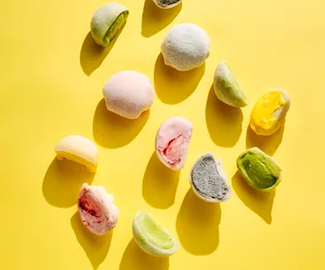 Pink, green, yellow and purple mochi-covered ice-cream on a bright yellow background