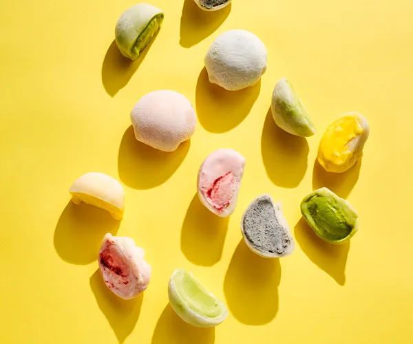 Pink, green, yellow and purple mochi-covered ice-cream on a bright yellow background
