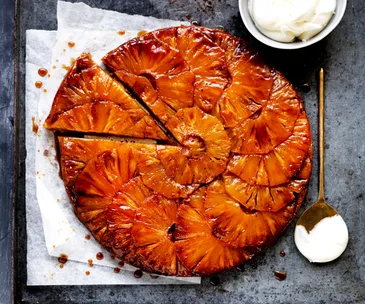 Upside-down tart with caramelised pineapple slices layered on top, with a triangular slice detached from the tart. 