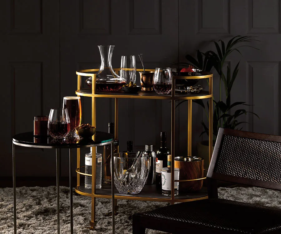 A two-level golden bar cart stocked with bottles of spirits, wine glasses and wine decanter.