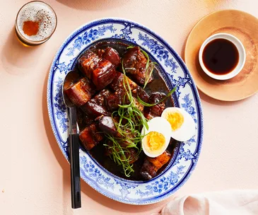 Overhead shot of a ornamental blur and white oval plate holding soy braised pork belly and a halved hard-boiled egg.