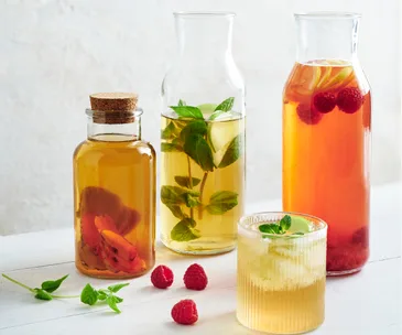 Three glass carafes plus a short ridged glass holding kombucha, garnished with mint and strawberries