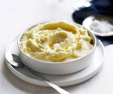 A white dish holding creamy mashed potato, with a grind of black pepper on top.