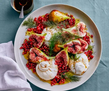 A large plate of figs with burrata, garnished with pomegranate arils and fennel sprigs 