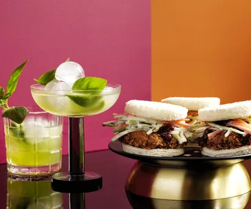 A basil gimlet served in a coupe glass, garnished with basil leaves.