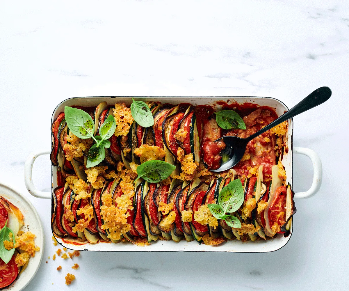 Thin slices of tomato, potato, eggplant, and zucchini layered horizontally in a shallow dish topped with toasted breadcrumbs.