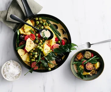 Generous chunks of eggplant, pineapple, tomatoes, snake beans, and pea eggplants in coconut curry sauce in a black saucepan.