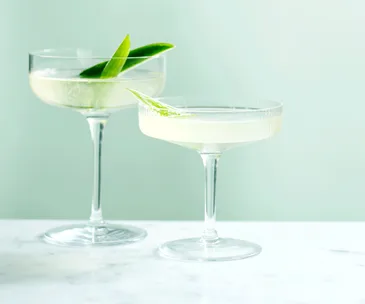 Two glasses of Ari Onassis cocktail garnished with two long slices of baby cucumber each