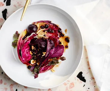 Bird's eye view of smoked beetroot dish with pink salad leaves in a white bowl atop a terrazzo surface