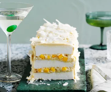 cross-section of meringue log cake coated in coconut flakes, displaying two yellow layers with mango chunks and 