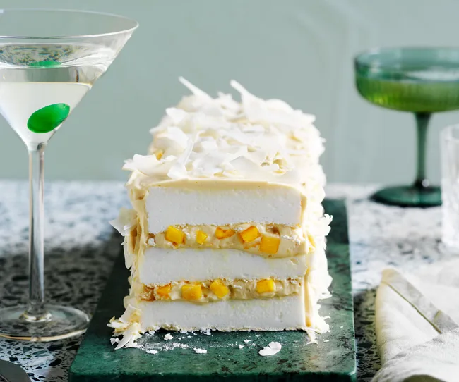 cross-section of meringue log cake coated in coconut flakes, displaying two yellow layers with mango chunks and