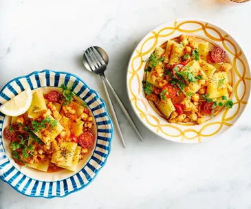 Two colourful bowls filled with paccheri pasta, tomatoes, prawns and herbs