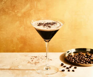 Single Espresso Martini in a martini glass next to a silver dish of coffee beans