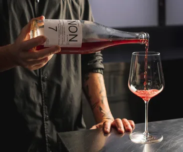 Person pouring bottle of red non-alcoholic liquid into a wine glass