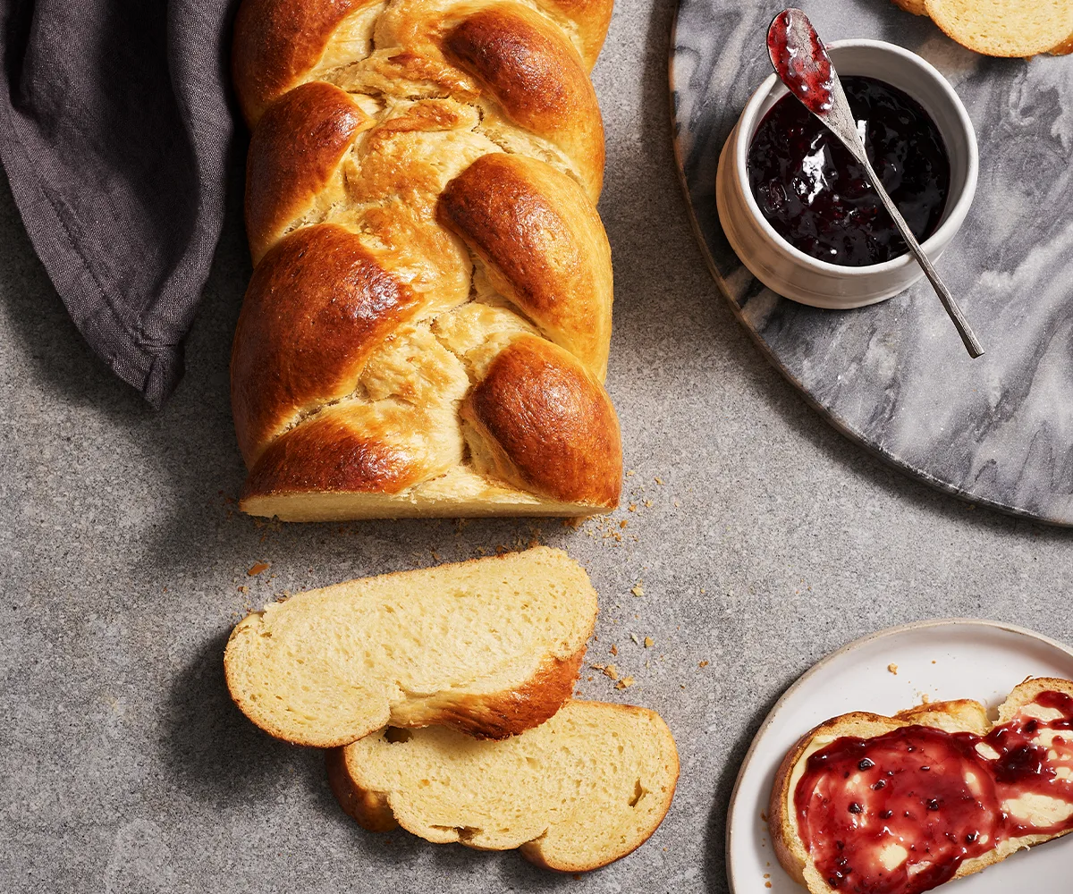 Aerial view of a golden plaited brioche loaf, sliced, with raspberry jam.