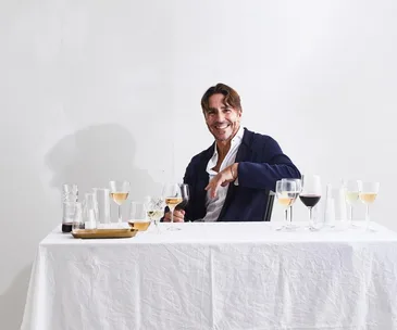 Portrait of Ned Goodwin with glasses of white and red wine on a white tablecloth-covered table