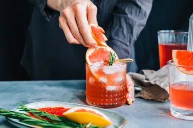 woman squeezing fresh orange slice into an orange cocktail 
