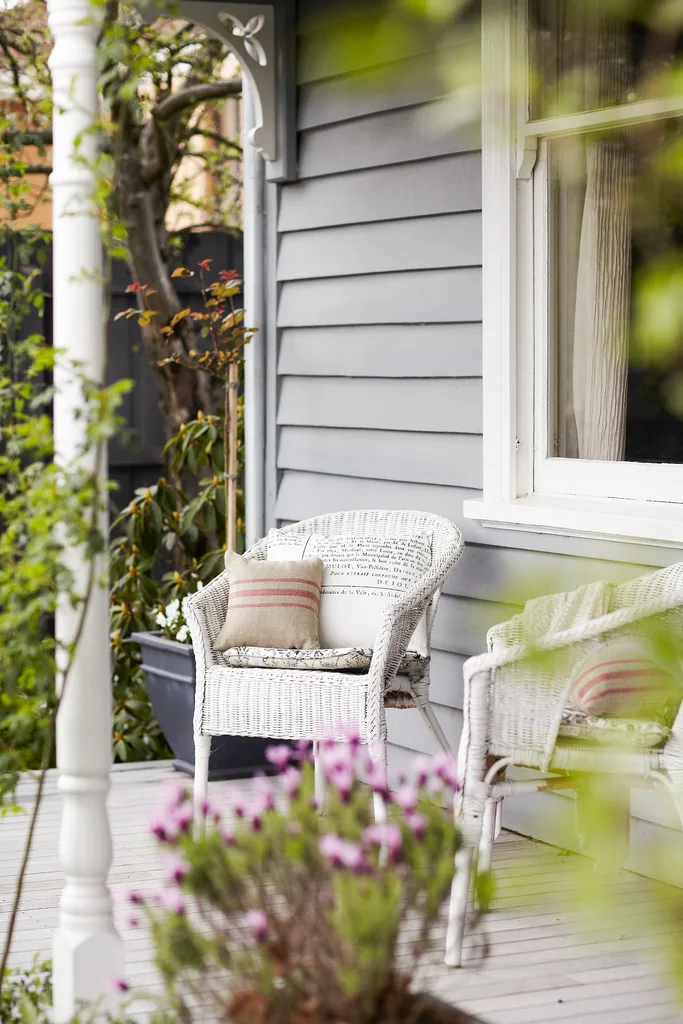 Wicker chairs on the verandah of a restored grey cottage.