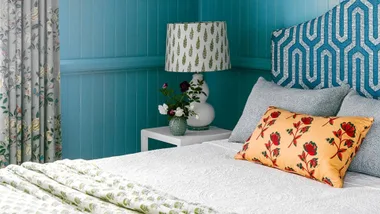 Blue bedroom with upholstered bedhead and patterned lampshade.