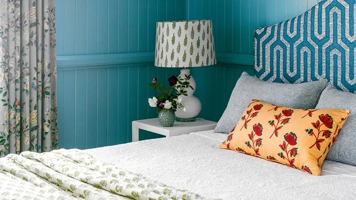 Blue bedroom with upholstered bedhead and patterned lampshade.