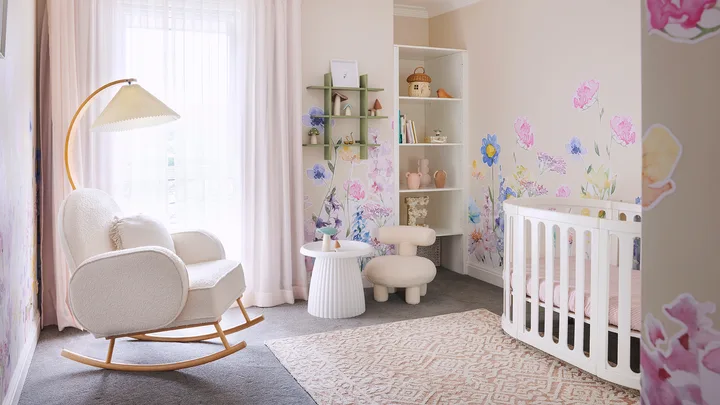 Girls nursery with neutral coloured walls, flower decals and white cot and boucle rocking chair.