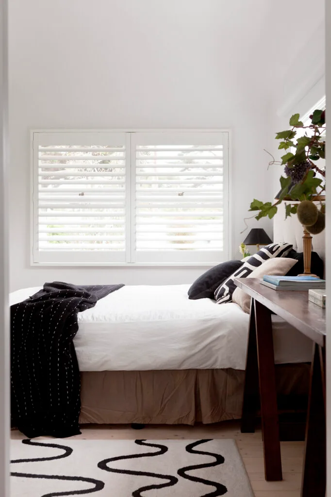 BLack and white bedroom with plantation shutters in a coastal weekender.