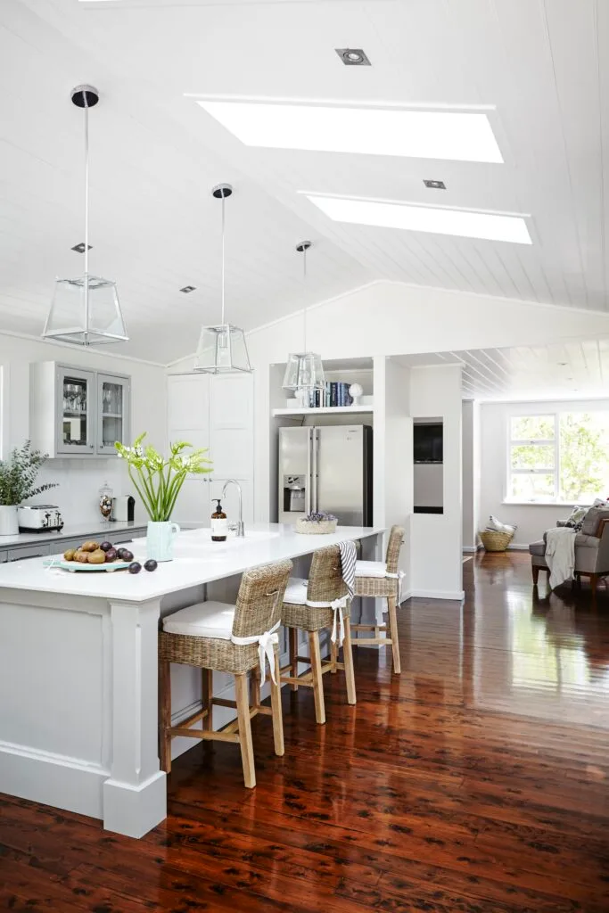 White country style kitchen with shaker cabinets and rattan bar stools.