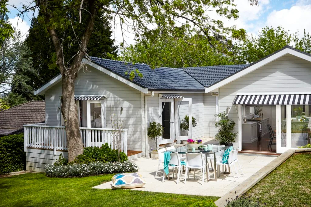 Exterior of a renovated cottage in Bowral with black and white awnings and alfresco dining area.