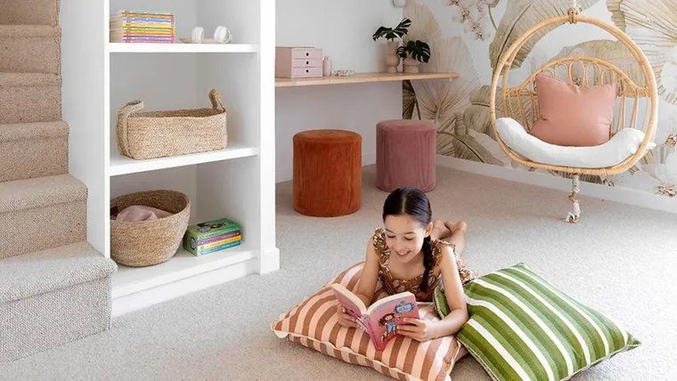 Girl reading book in organised kids play room filled with storage baskets and other toy organisation solutions.