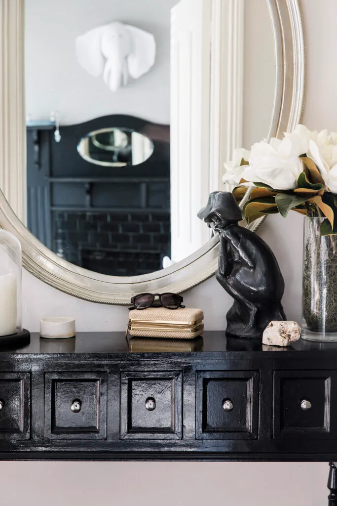 Black hallway table and mirror with fresh flowers and other decorative knickknacks on top.