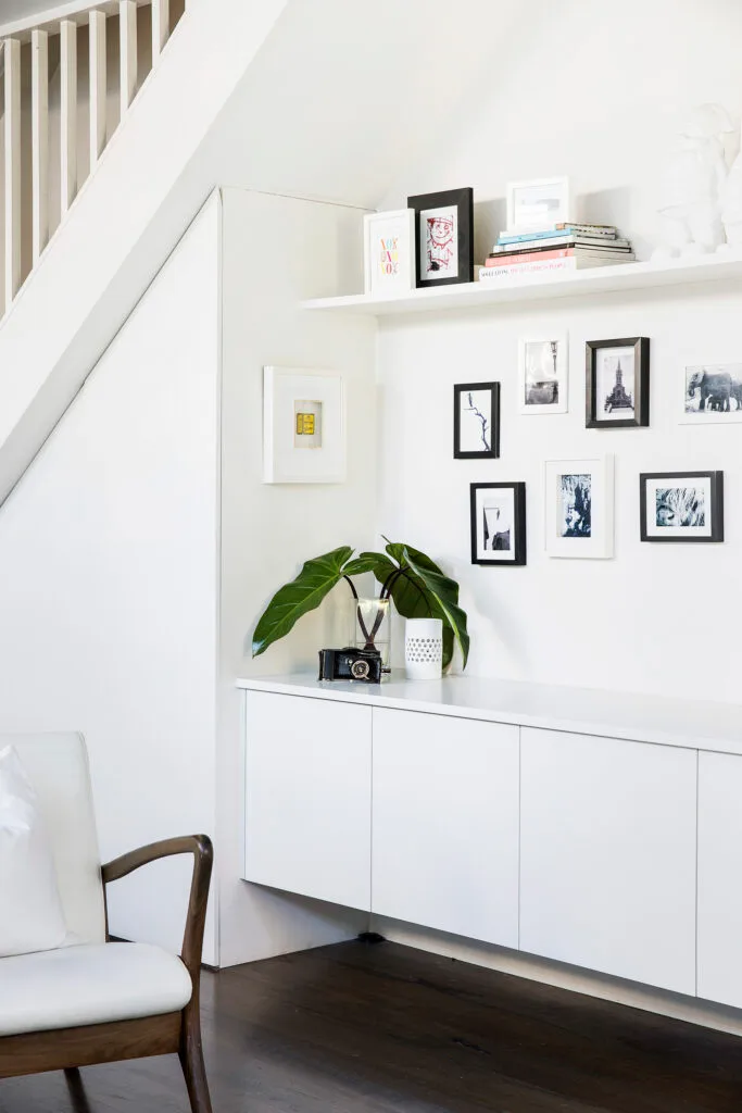 Cavity under the stairs styled with white floating joinery and a gallery wall.