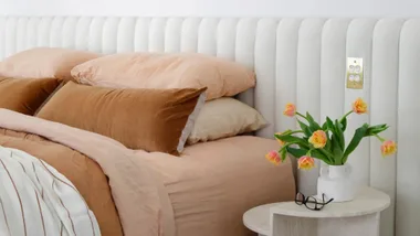 Contemporary bedroom with upholstered bed head, neutral sheets and vase of tulips on the bedside table.