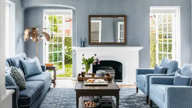 a blue living room with a mirror above a white fireplace to demonstrate feng shui mirror placement guidelines