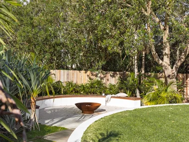 Coastal, tropical garden with curved wall, fence and lawn.