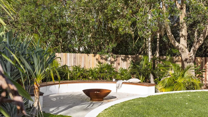 Coastal, tropical garden with curved wall, fence and lawn.