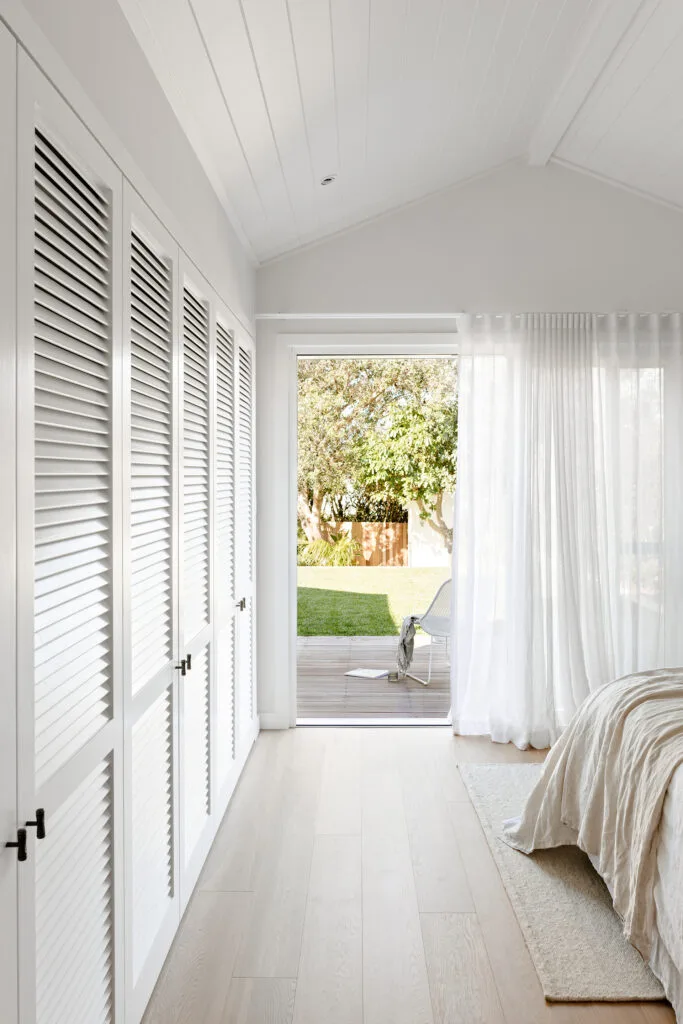 Coastal style bedroom with exterior door, and wardrobe doors with louvred fronts.