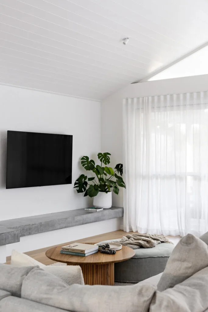 White and concrete beach house living room with pitched roof and sheer curtains.