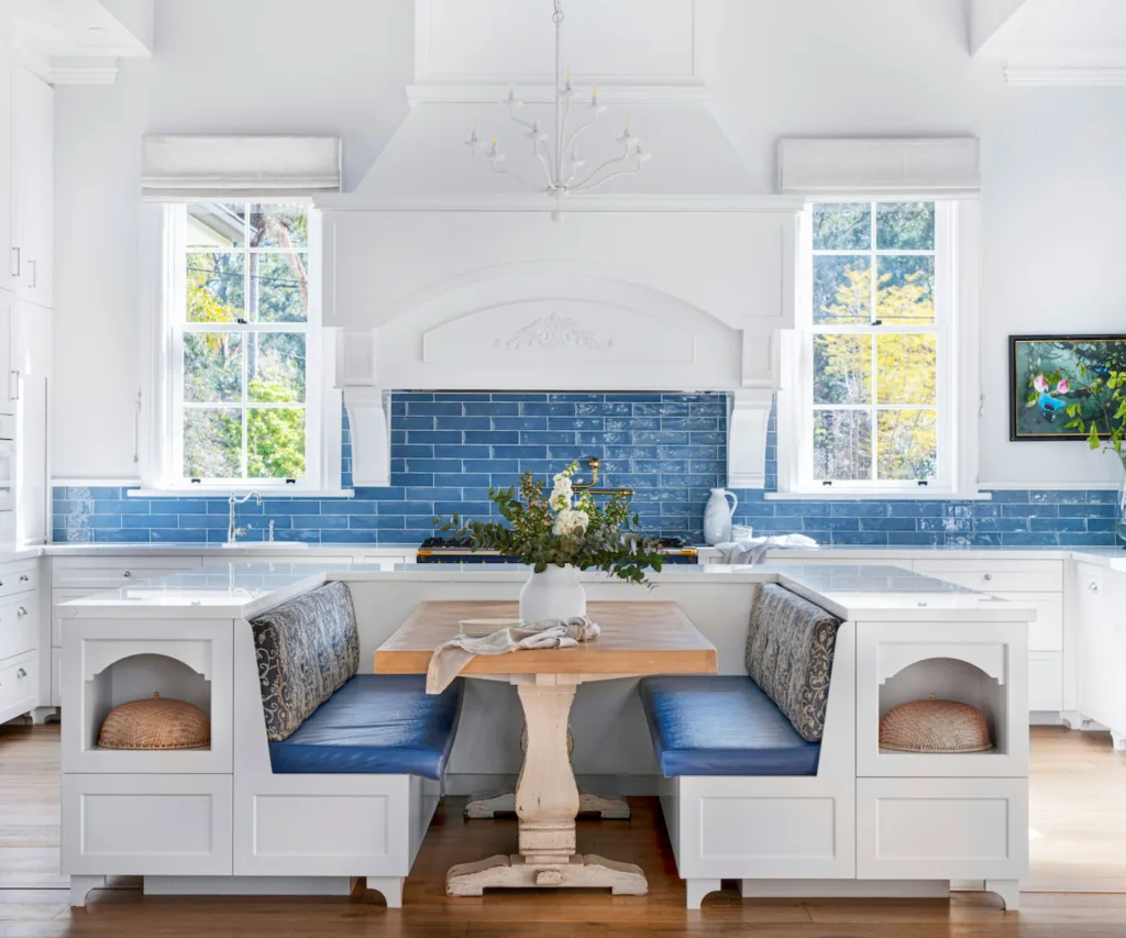 Banquette seating with blue cushions in front of a kitchen with a blue tiled splashback