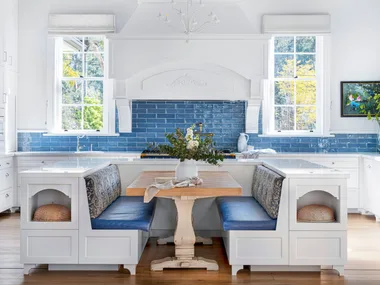 Banquette seating with blue cushions in front of a kitchen with a blue tiled splashback