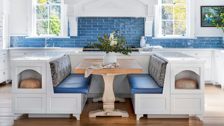 Banquette seating with blue cushions in front of a kitchen with a blue tiled splashback