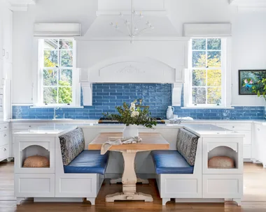 Banquette seating with blue cushions in front of a kitchen with a blue tiled splashback