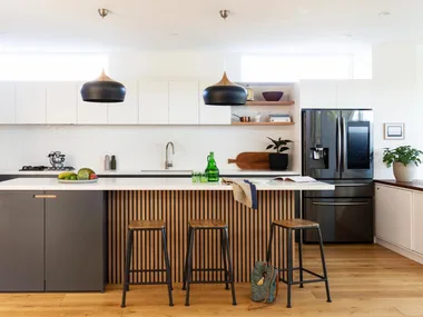 Modern kitchen with black pendant lights, wooden island, bar stools, marble countertop, and stainless steel appliances.