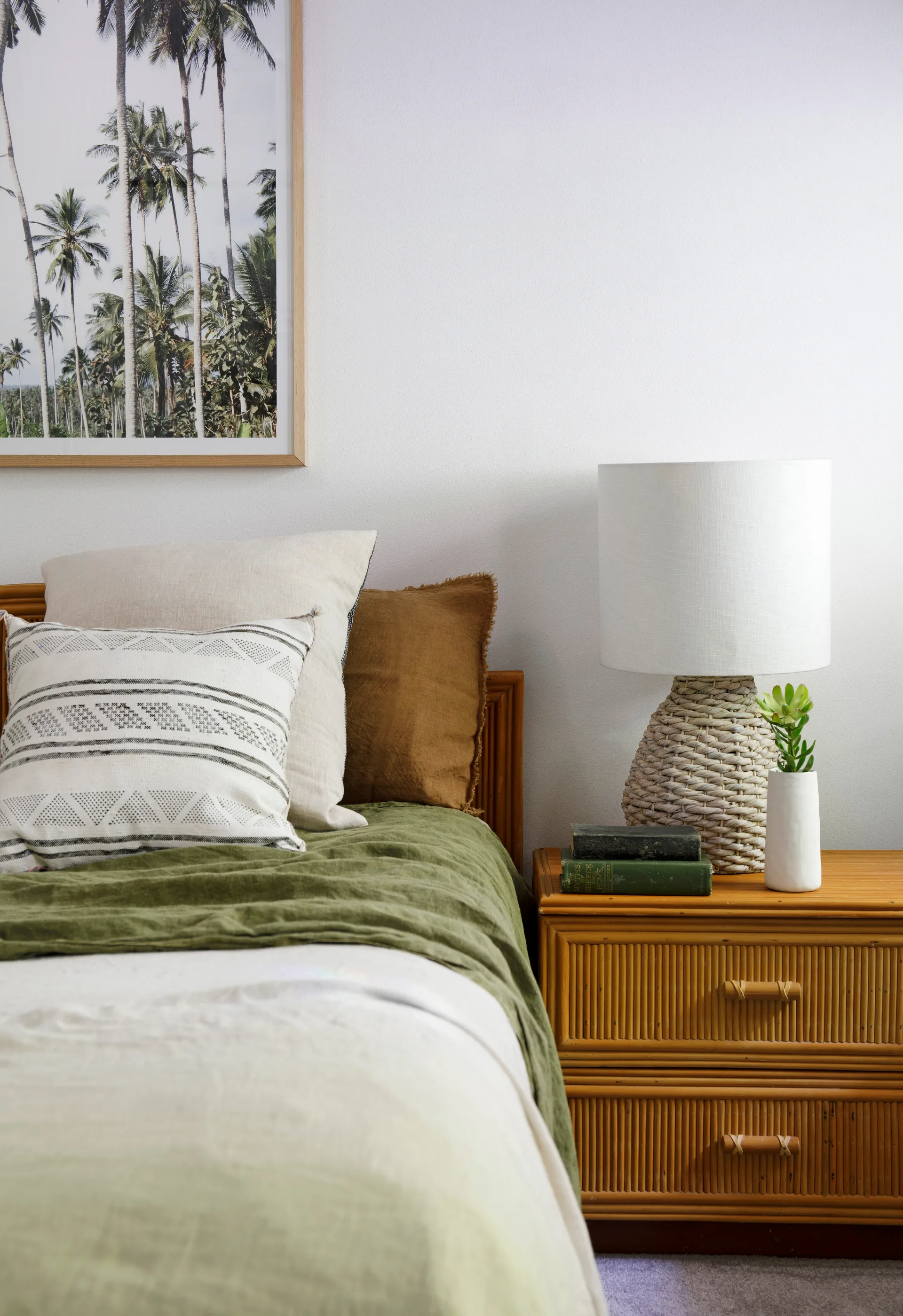bedroom with linen bedding in multiple shades of green with timber side table and lamp