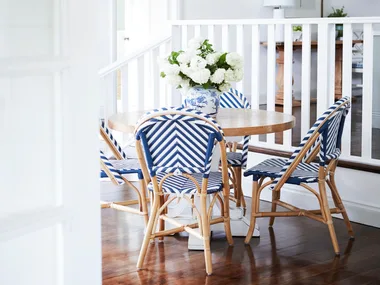 A round timber dining table set with four blue Parisian style chairs.