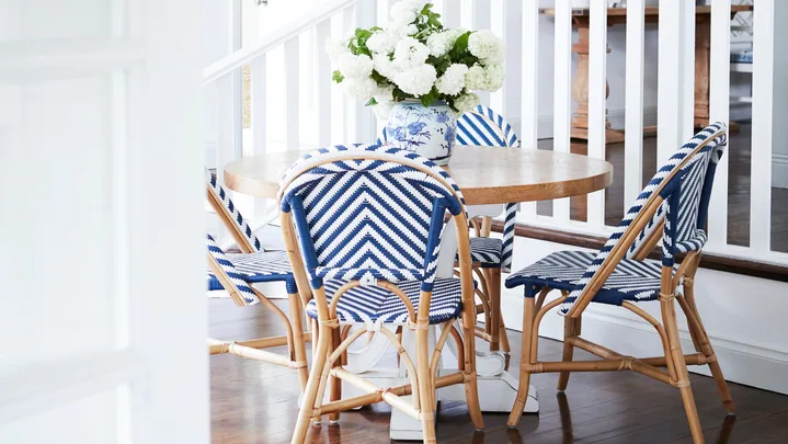 A round timber dining table set with four blue Parisian style chairs.