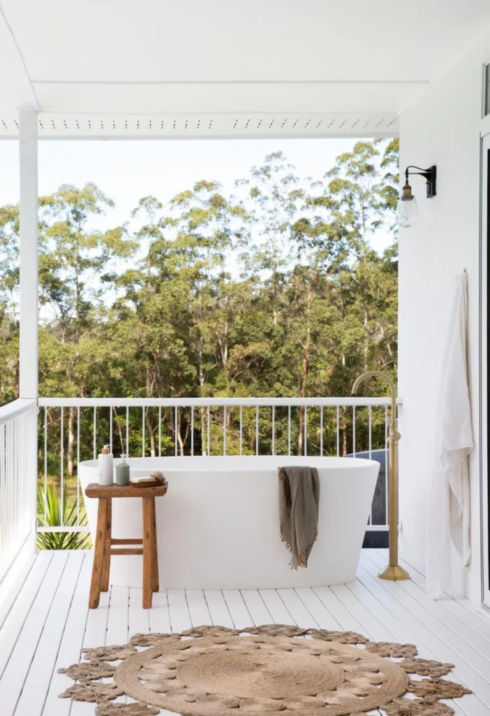 Freestanding bath tub on an outdoor balcony with a sisal rug in the foreground.