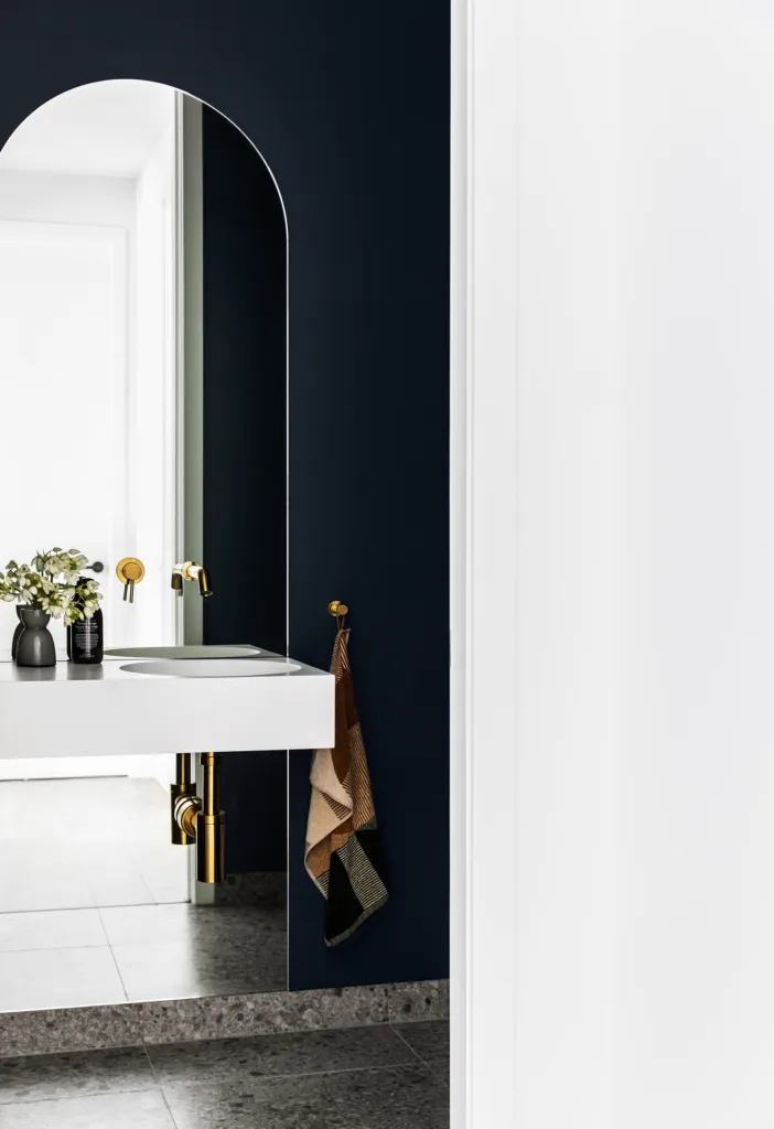 Dark blue painted powder room with tall arched mirror