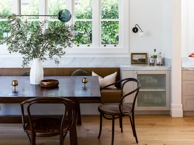 Dark brown leather banquette seating with a large dining table and dining chairs against a white wall